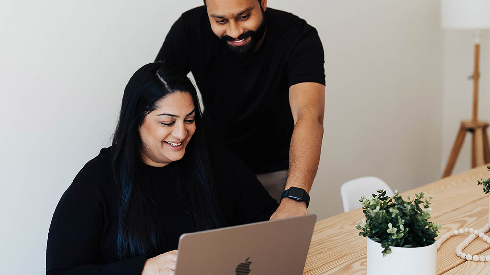 two people looking at a laptop screen together, smiling